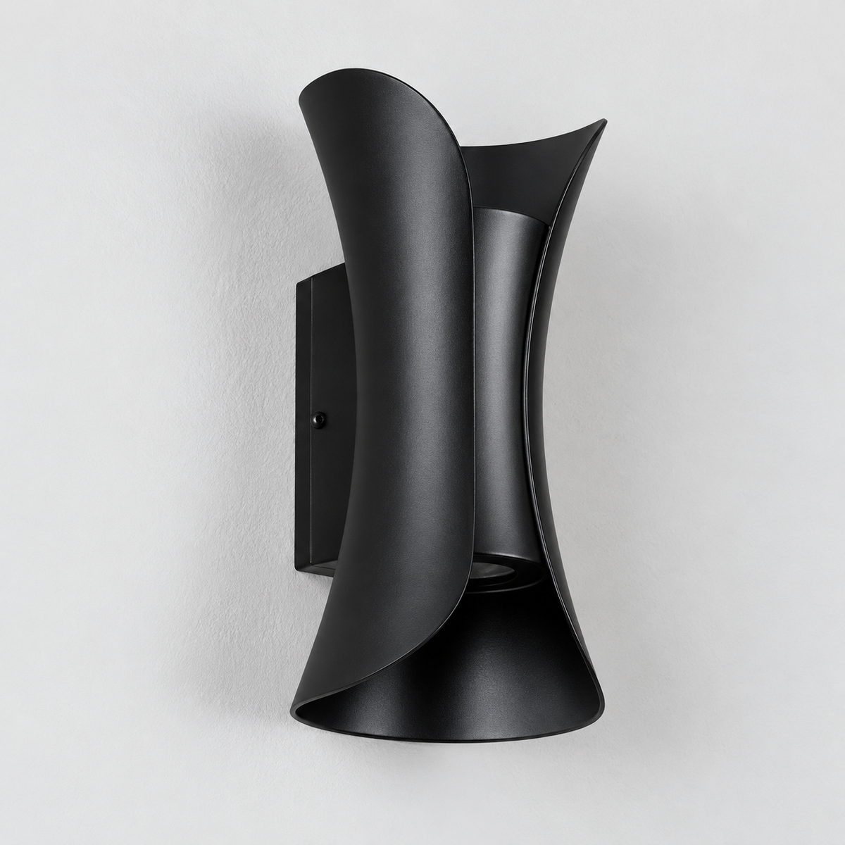 A modern matte black wall sconce with a sculptural, curved design mounted on a light gray textured wall.