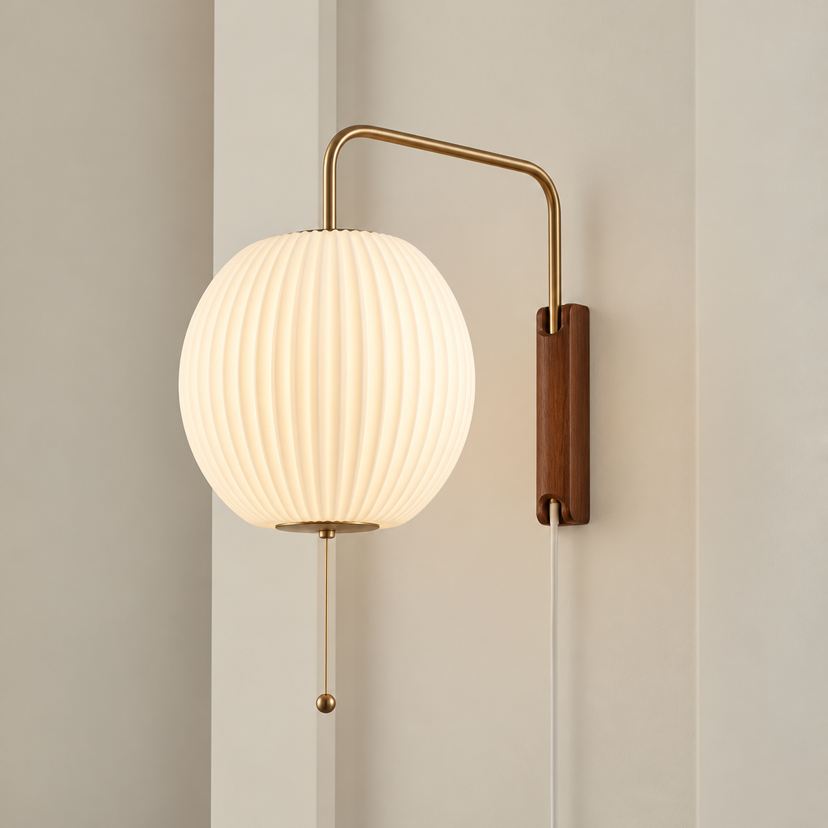 A modern wall-mounted sconce with a ribbed white globe shade, a curved brass metal arm, a vertical brown wood-look wall plate, and a hanging pull chain, shown lit against a beige wall.