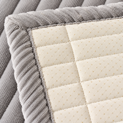 Close-up of a mattress or bedding corner showing a gray ribbed plush border around a cream quilted top surface with a subtle dotted texture.