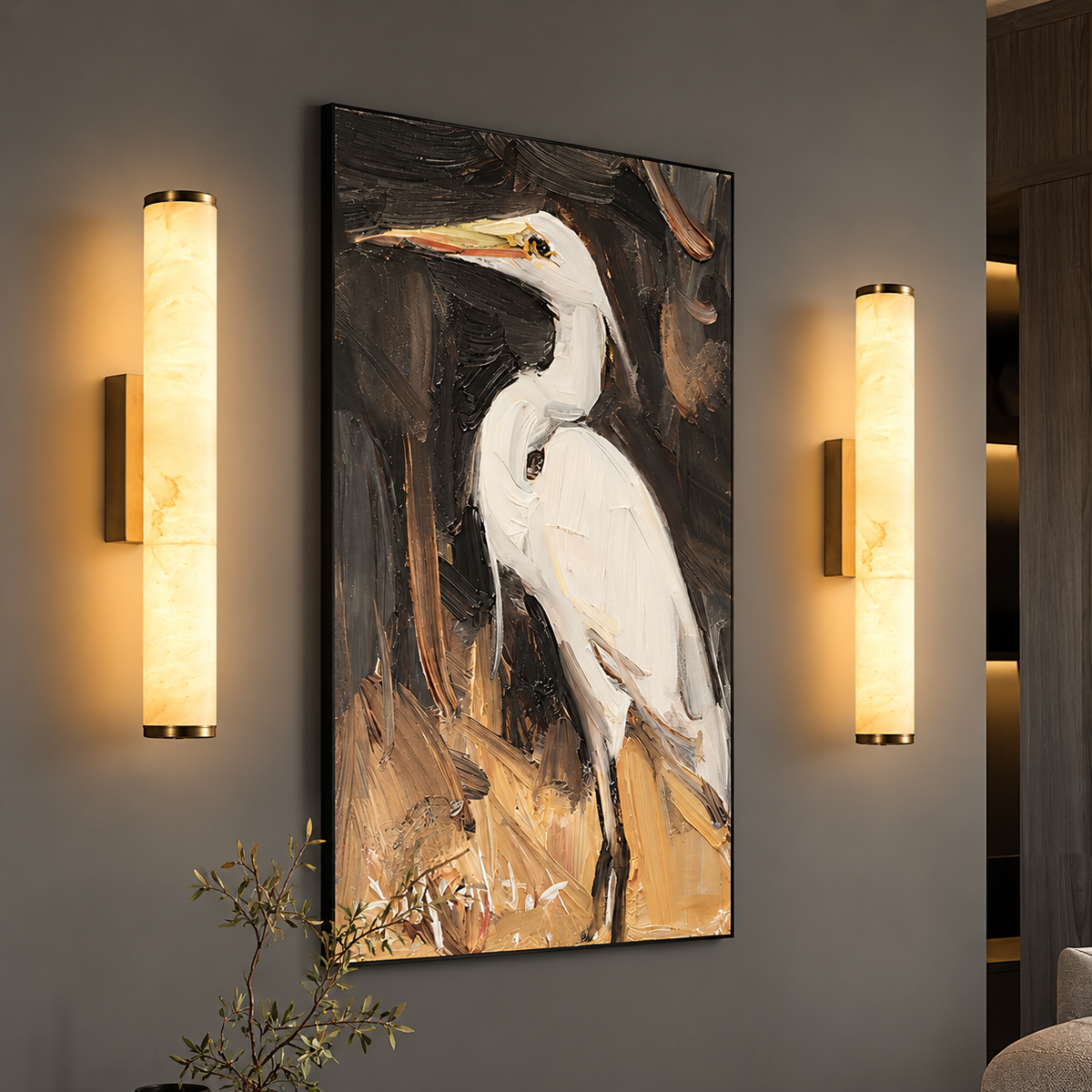 A vertical framed wall art print depicting a white heron on a dark, painterly background, displayed on a gray wall between two illuminated cylindrical wall sconces.