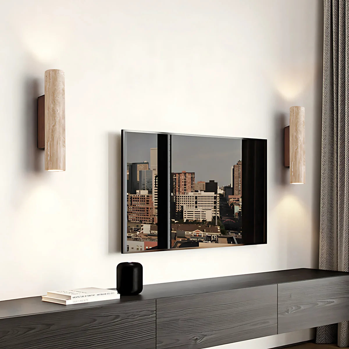 A modern wall-mounted TV with a mirrored finish reflecting a city skyline, flanked by two cylindrical wall sconces on a white wall above a dark wood console.