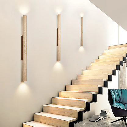 Three modern wall sconces with vertical light wood posts and dark center panels are mounted on a cream wall above a wooden staircase. A teal chair is partially visible in the lower right corner.