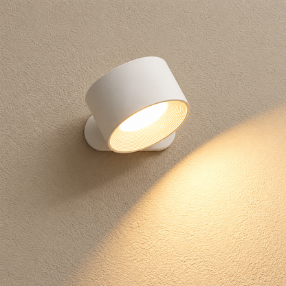 A modern white cylindrical wall sconce light fixture mounted on a textured beige wall, casting a warm yellow glow downward and to the right.