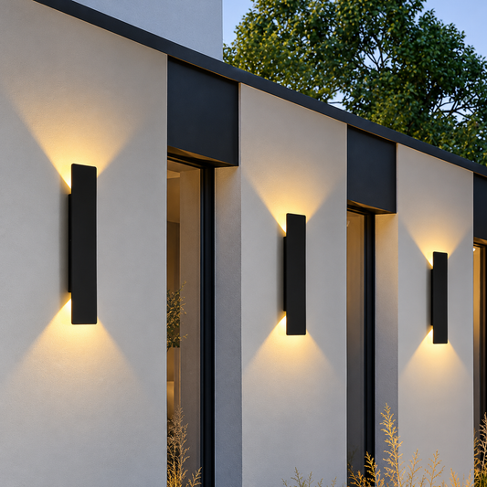 Three modern black rectangular wall sconces mounted on the exterior of a minimalist beige building, casting a warm yellow light downward.