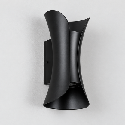 A modern matte black wall sconce with a sculptural, curved design mounted on a light gray textured wall.