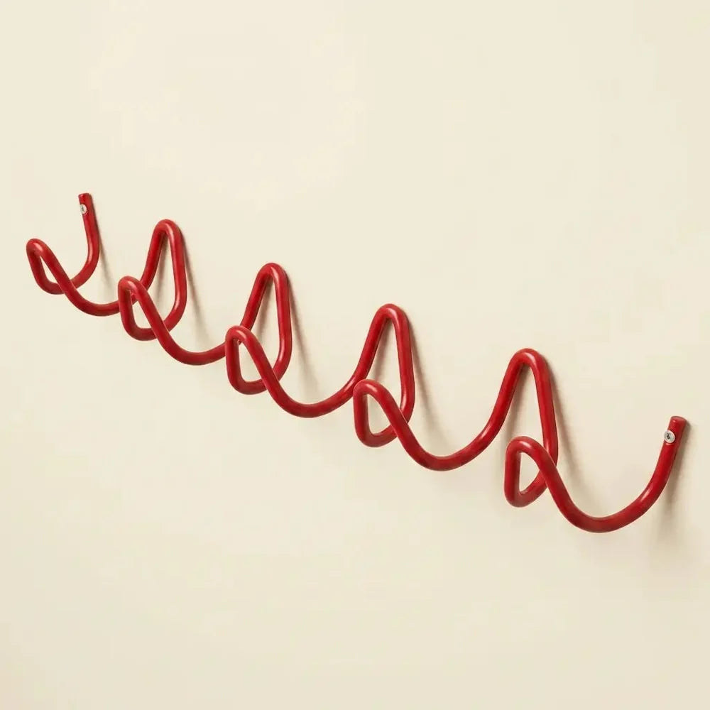 A red wavy metal wall hook mounted on a plain beige wall.